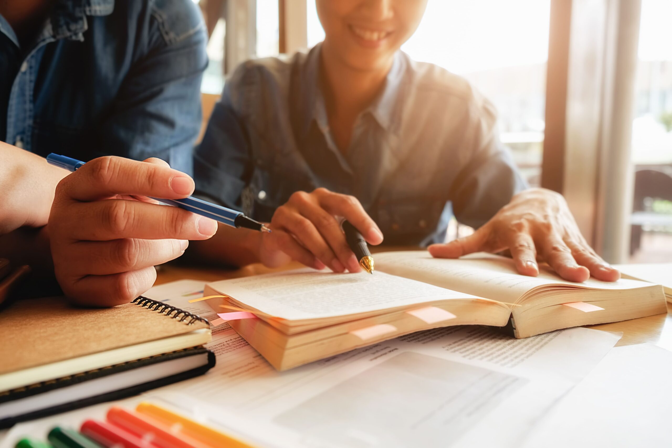 Duas pessoas concentradas, partilhando conhecimento enquanto estudam juntas num caderno.