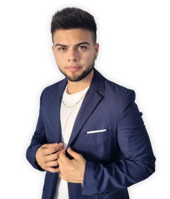 Gen Contreras (1) Homem com barba e cabelo penteado para cima, usando um blazer azul marinho sobre uma camiseta branca.